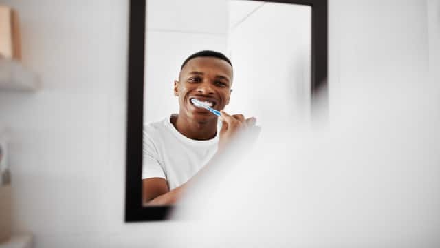 Young man brushing his teeth in front of bathroom mirror 