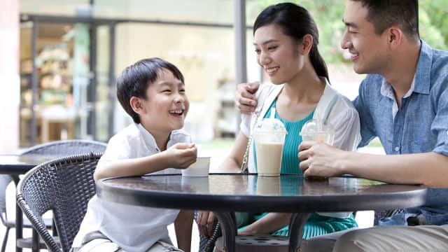 a mother and father smiling sitting down and enjoying drink with their son