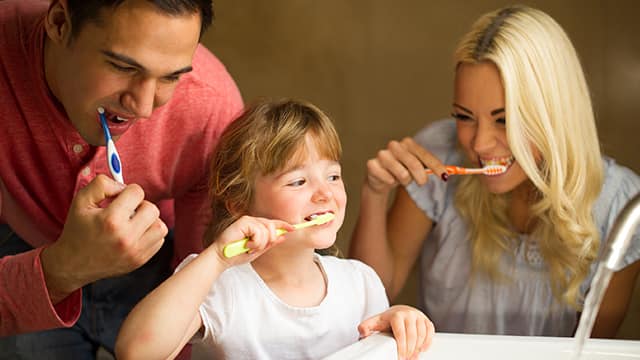 Padres enseñándole a su hija a lavarse los dientes