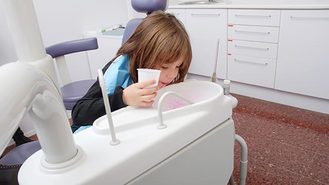 a girl at the dentist spitting water in the dental chait sink