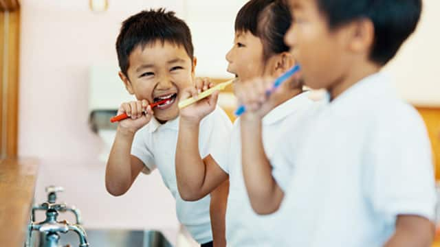 Three kids brushing their teeth over the sink