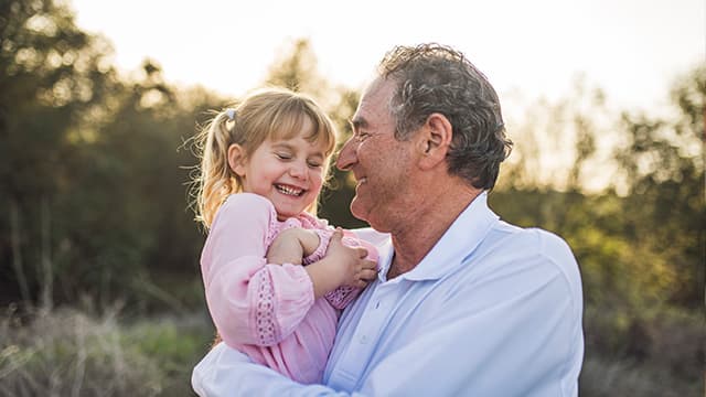 Grandpa holding granddaughter in field and laughing