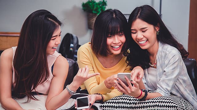 three Asian girls smiling while looking at phone 