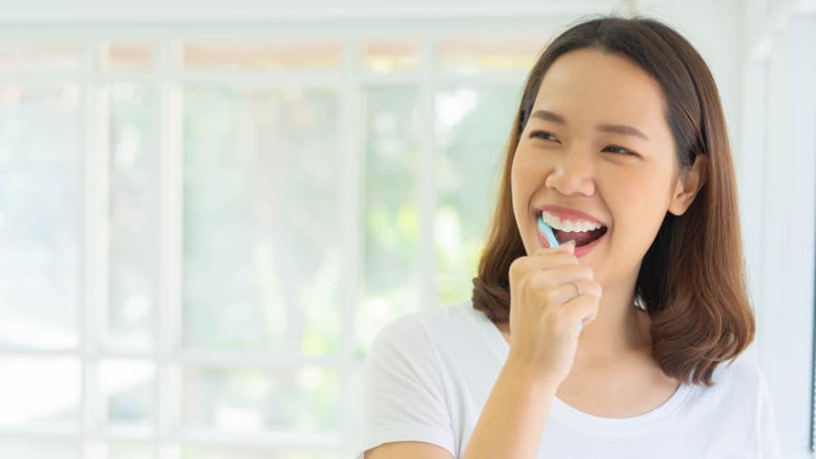 A woman brushing her teeth in front of the bathroom mirror