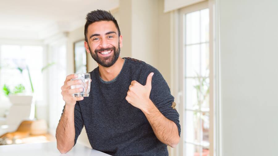 An older man smiling while holding a glass of water 