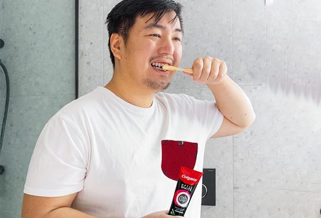 Man brushing his teeth using a bamboo toothbrush and Colgate Optic White O2 toothpaste