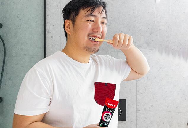 Man brushing his teeth using a bamboo toothbrush and Colgate Optic White O2 toothpaste Man brushing his teeth using a bamboo toothbrush and Colgate Optic White O2 toothpaste