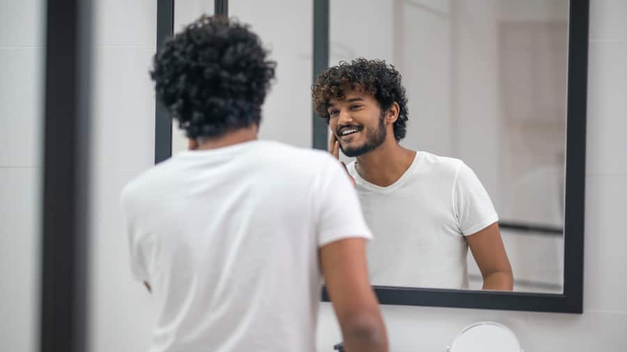 A happy young man looking confident in the mirror after teeth cleaning at home A happy young man looking confident in the mirror after teeth cleaning at home