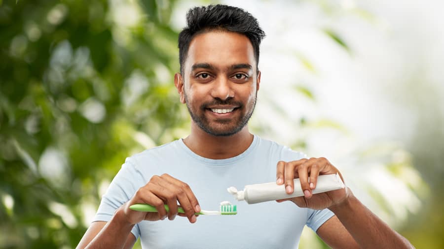 a man smiling putting on Colgate toothpaste onto a toothbrush