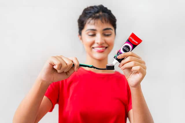 Woman putting Visible White O2 teeth whitening toothpaste on a toothbrush