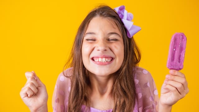 Niña sonriente con sus nuevos dientes definitivos comiendo helado