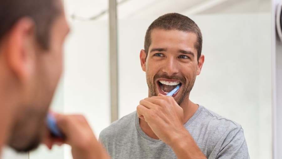 Hombre joven cepillándose los dientes frente al espejo del baño