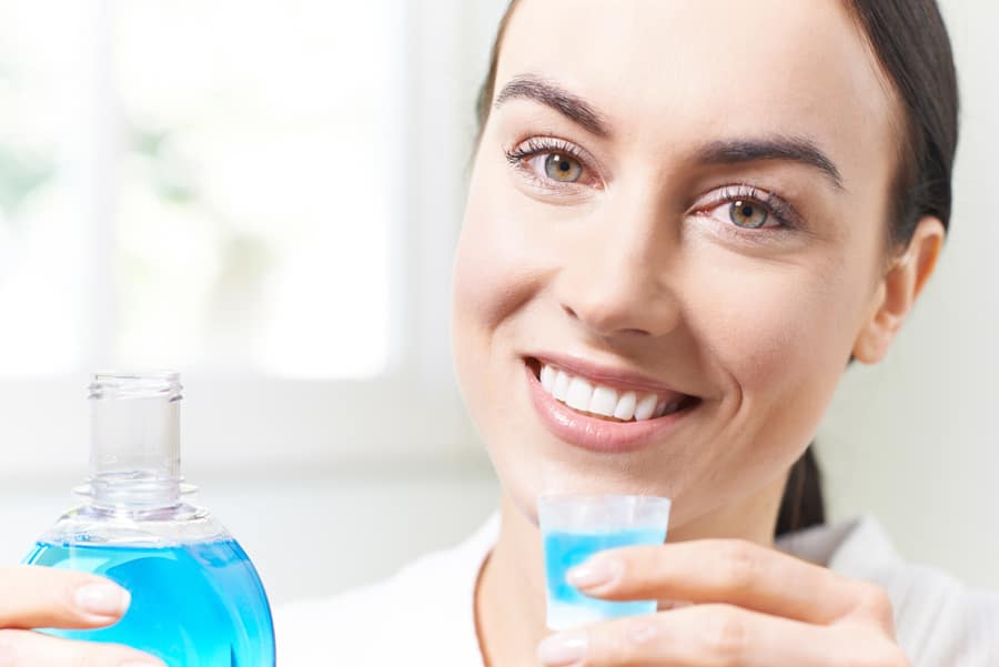Mujer limpiándose los dientes con enjuague bucal