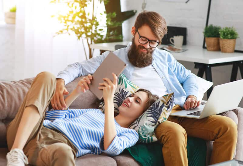 Happy couple relaxing at home with laptop and tablet