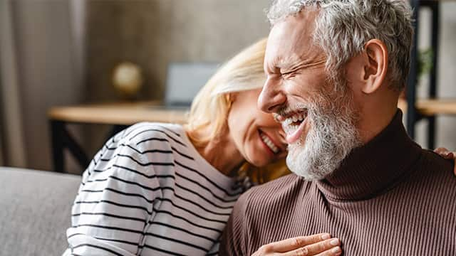 happy laughing middle aged couple bonding while relaxing sitting on sofa