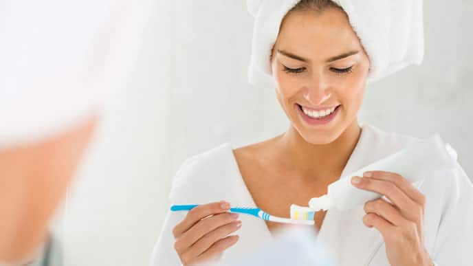 a woman smiling brightly while applying Colgate toothpaste onto her toothbrush