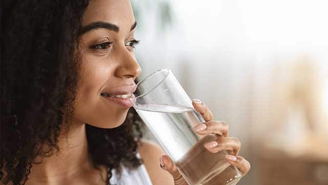 Smiling Black woman drinking water from glass and looking away.