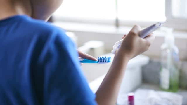 close-up of a young person squeezing toothpaste onto a toothbrush.