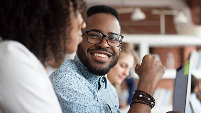 Smiling African American male employee look at colleague chattin