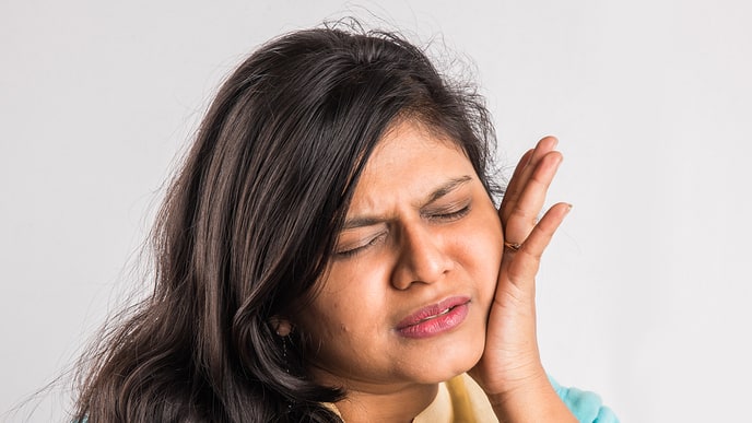 Woman grimacing in pain holding her cheek, representing the need for effective toothache medicine Woman grimacing in pain holding her cheek, representing the need for effective toothache medicine