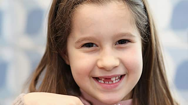 Niña sin dientes cepillándose los dientes