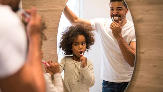 Brushing teeth with dad Young child brushing their teeth with dad in front of the bathroom mirror