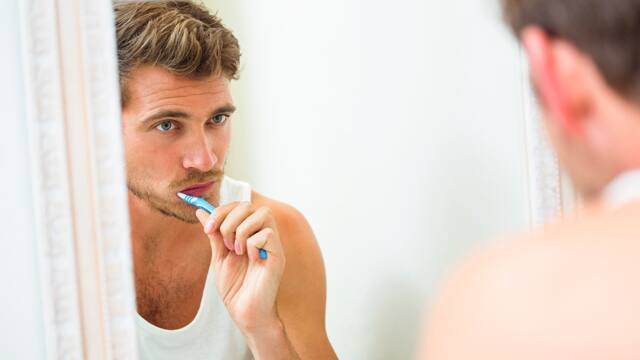 man-looks-in-the-mirror-while-brushing-his-teeth.jpg