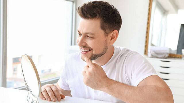 Man with healthy teeth looking in mirror at home