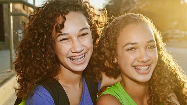 two girls are smiling and hugging as they stand outside