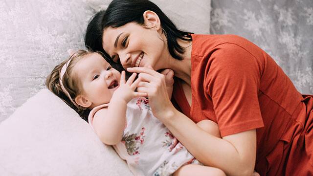 Young mother and her baby laying down next to each other while smiling 