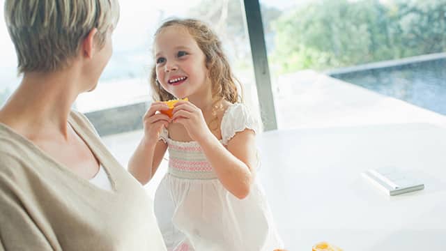 Mother watching girl eating orange Mother watching girl eating orange