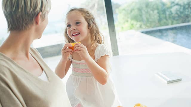 Mother watching girl eating orange