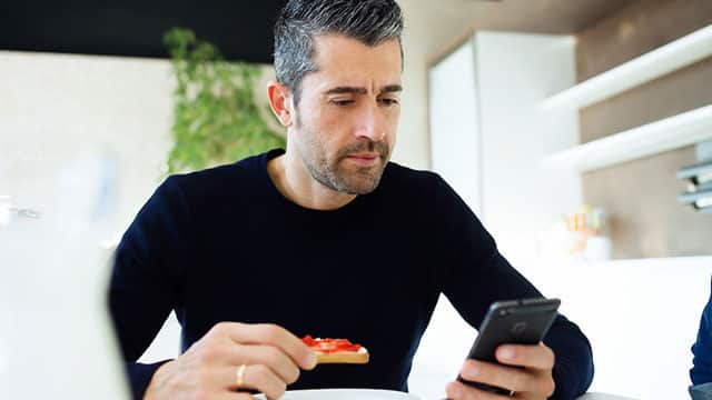 man looking at his phone while eating a piece of bread