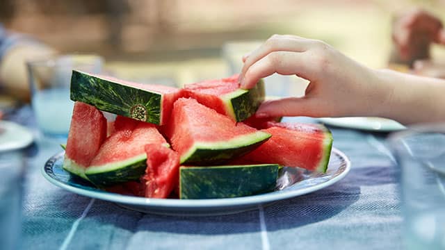 A close up of the hand reaching for a watermelon slice