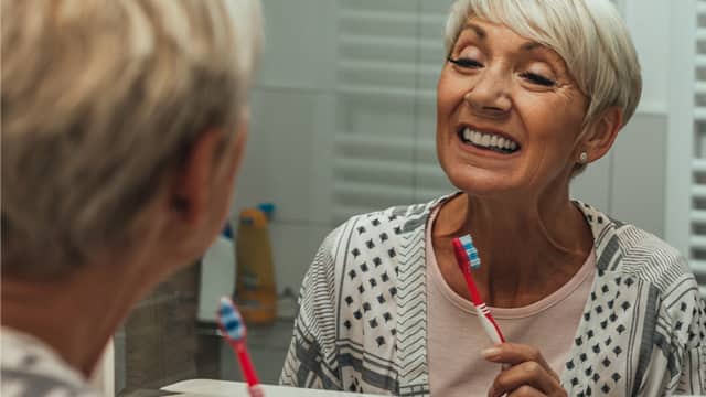 a senior woman examines her gums and teeth in a mirror while brushing a senior woman examines her gums and teeth in a mirror while brushing