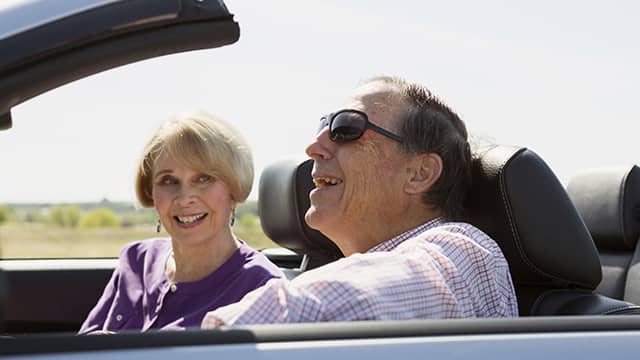 an elderly couple smiling while driving on a convertible