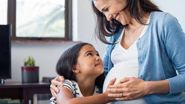 daughter holding her smiling pregnant mother belly