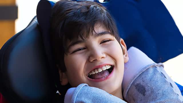 Smiling child in his wheelchair with support pillows around his neck 