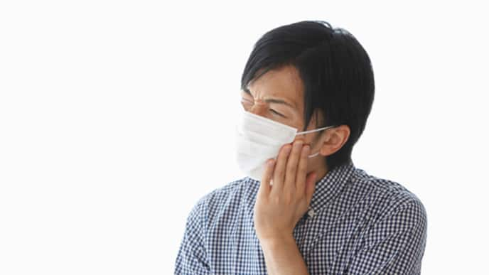 man wearing a mask holding his cheek in pain