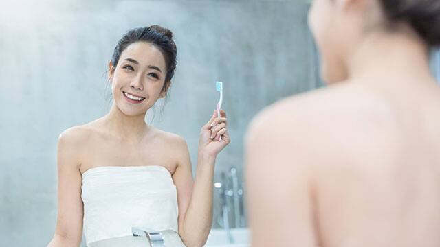 Young woman is looking at the mirror while holding a toothbrush