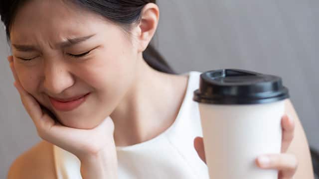 a woman holding her jaw from pain while holding a cup of coffee