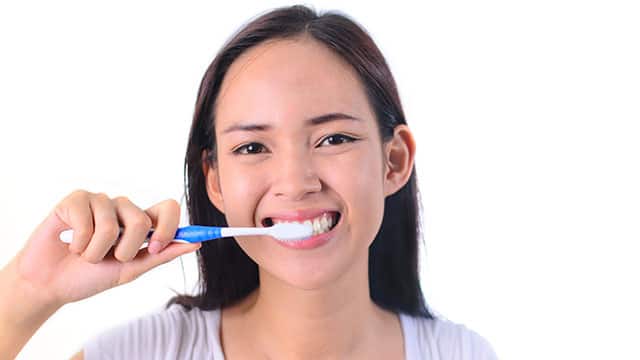 Woman brushing her teeth with Colgate to help with bleeding gums