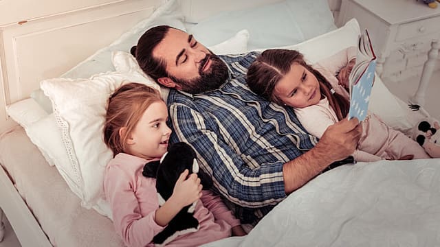 father reading a book to his daughters