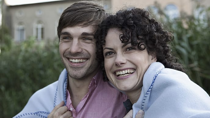 A man and a woman smiling covered with blanket outdoor