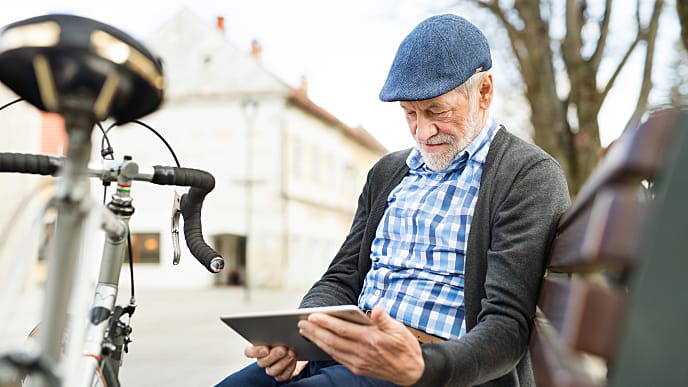 Senior man in town sitting on bench working on tablet