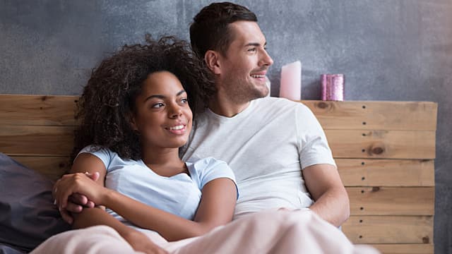  a young couple is sitting on bed at home