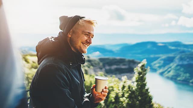 hipster tourist hold in hands mug of hot drink, lonely guy smile enjoy sun flare mountain in auto, happy traveler drink cup of tea on nature, vacation weekend concept on panoramic landscape