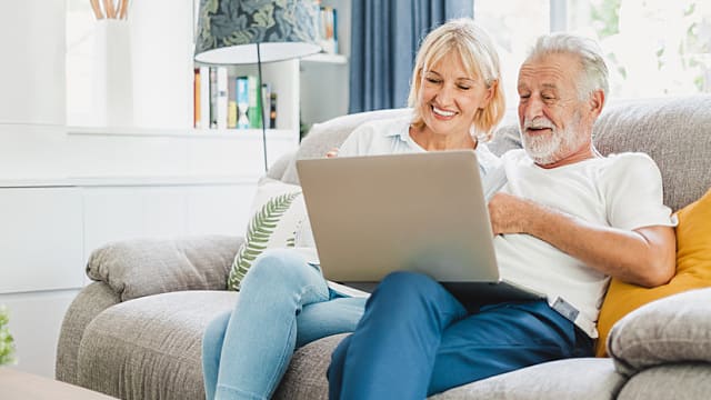 Couple senior using computer laptop on sofa at home for online shopping, surfing internet