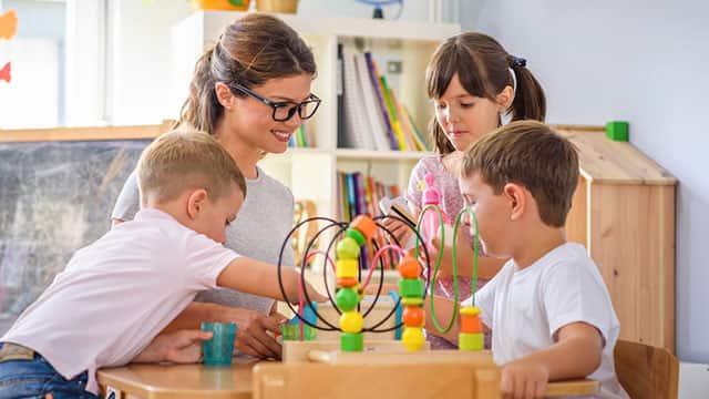 a female teacher smiling at three children playing