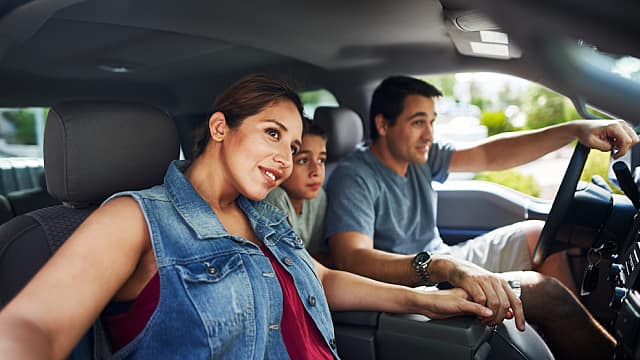 hispanic family with mother, father and son sitting in truck looking outside